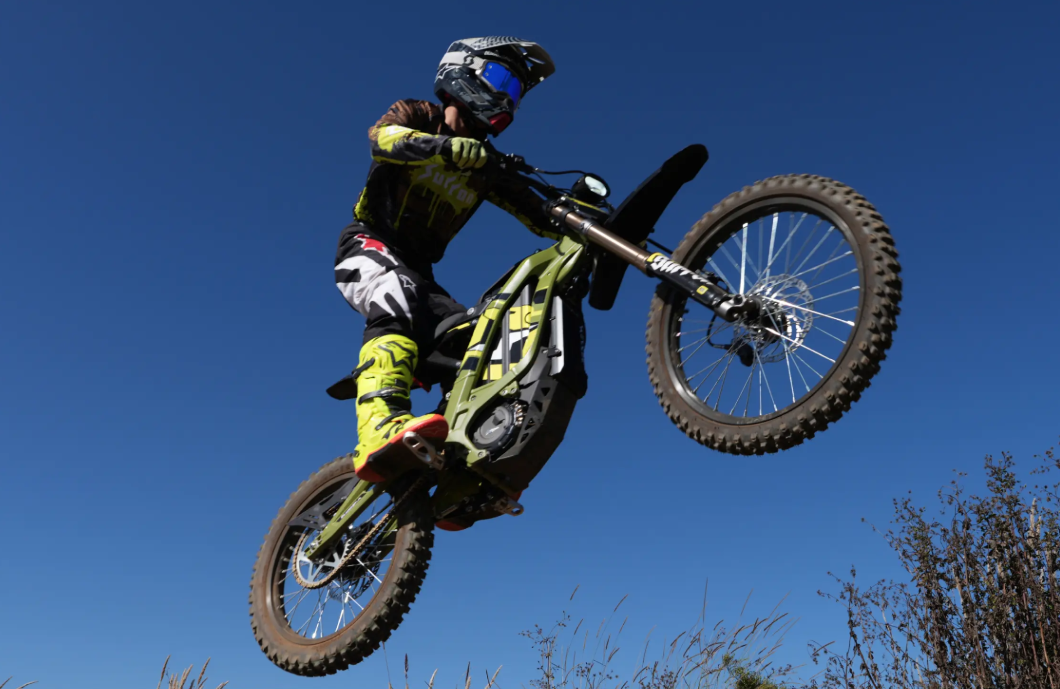 Person on a Sur-Ron light bee x performing a stunt against a clear blue sky