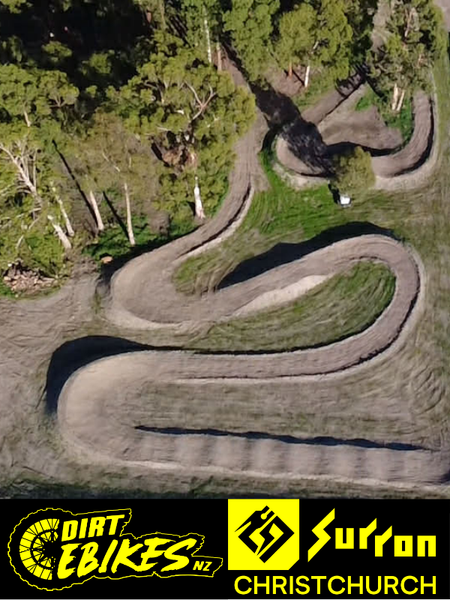 Winding dirt bike track surrounded by trees with 'Dirt Ebikes NZ' and 'Surron Christchurch' logos at the bottom.