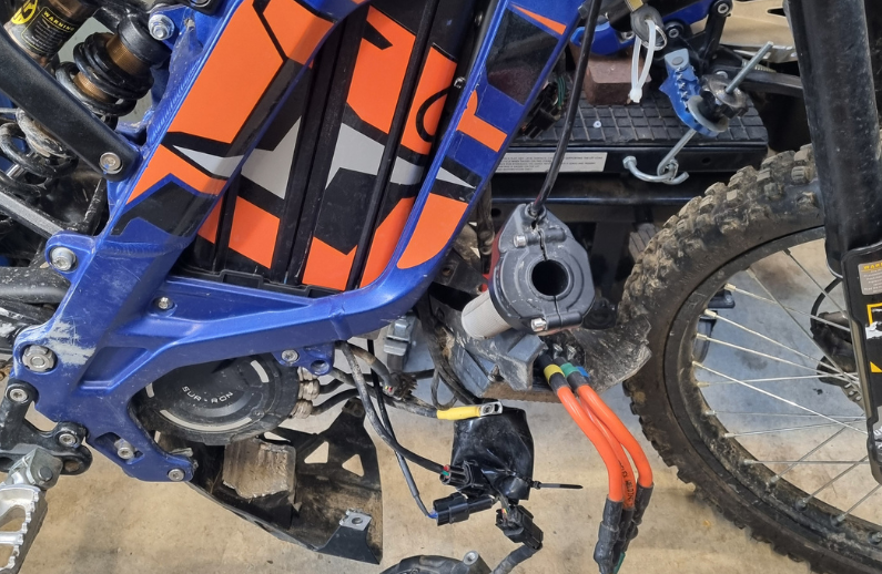 Close-up of a dirt bike's suspension and chain area with orange and black components.