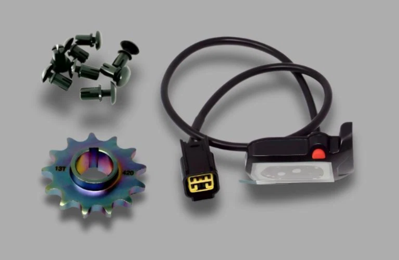 Genuione Surron parts including a colorful gear, connectors, and a cable on a gray background