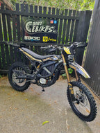 Electric dirt bike in front of a branded fence with 'Dirt E Bikes NZ' and 'Surron' logos.