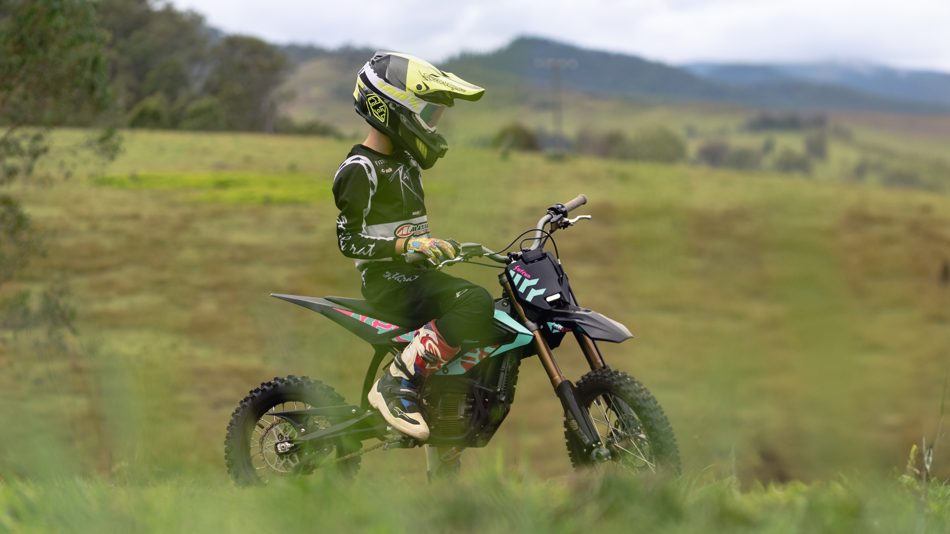 Person on a surron electric dirt bike in a grassy field with mountains in the background