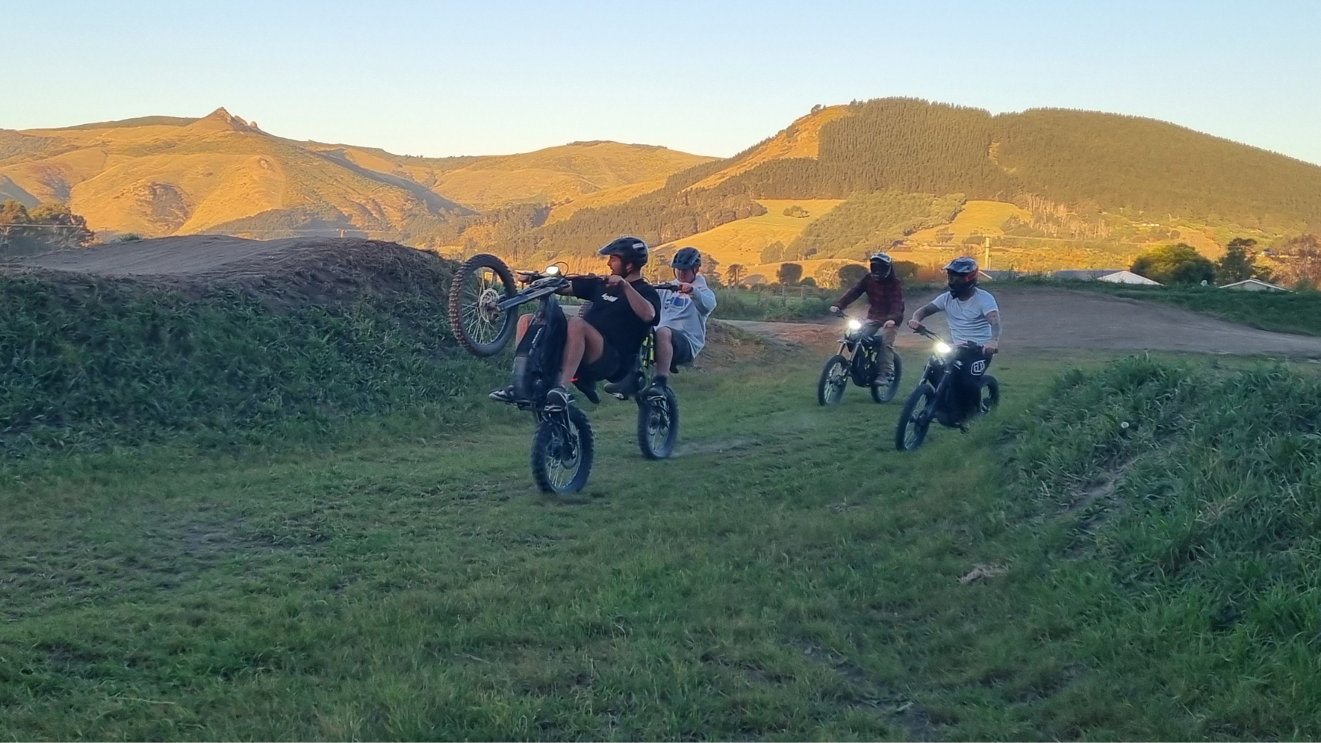 Dirt EBikes, Surron Christchurch hero Image - People riding motorcycles on a grassy hill with mountains in the background